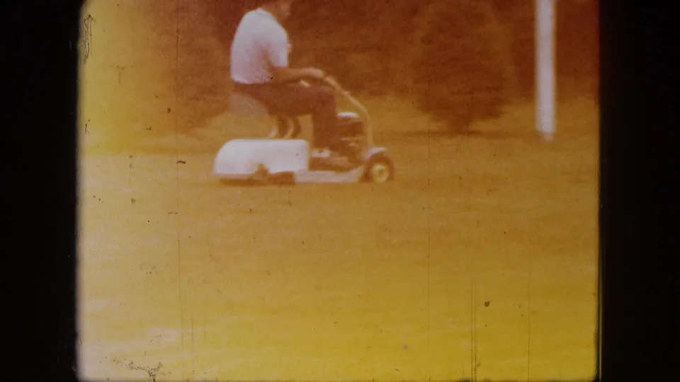The mower and seated operator pass through the frame in faded 8mm footage from the 1963 Saint Paul yard scene.