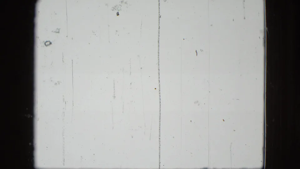 A pale leader-like or overexposed 8mm frame shows vertical scratches, dust marks, and dark gate edges after the mowing scene.