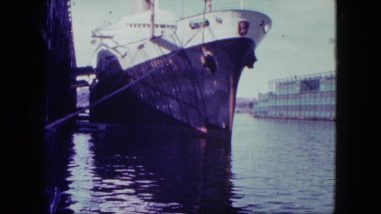 1963 San Diego home-movie frame showing a large ship moored at port, seen from a shaded dockside angle across harbor water.