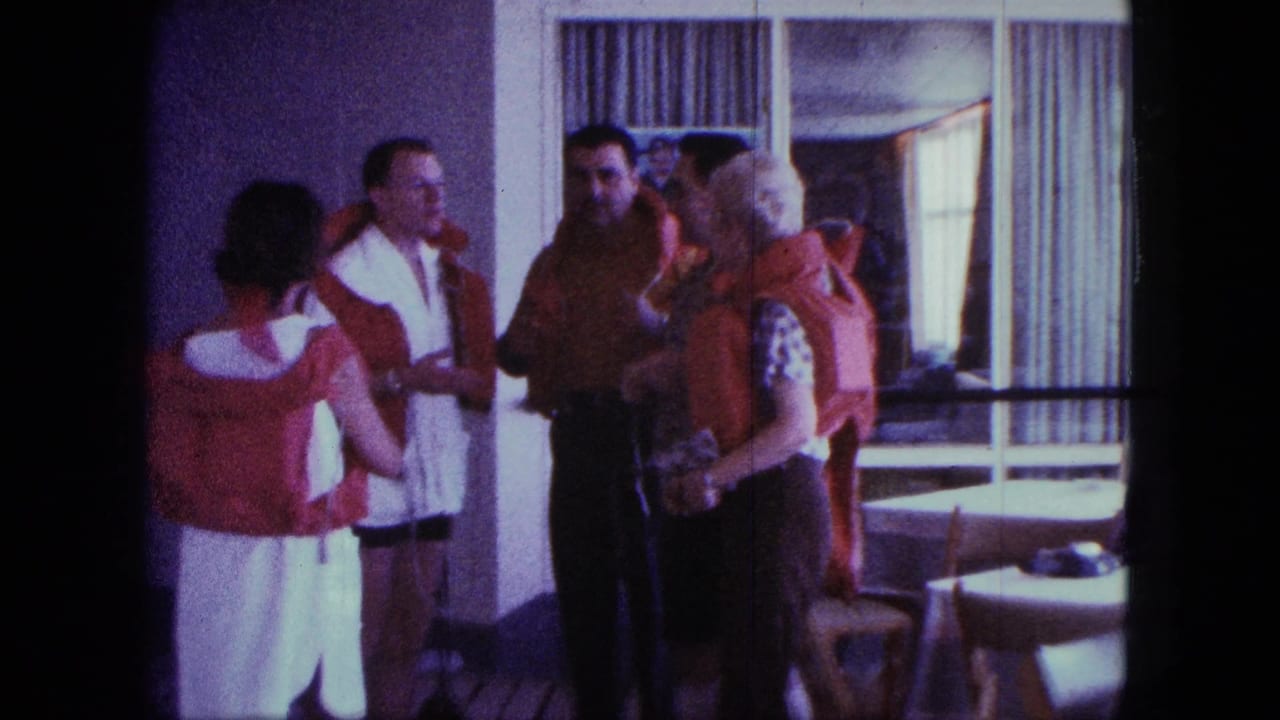 Adults in life jackets converse inside a shipboard-looking room, with curtains, windows, tables, and chairs visible in the background.
