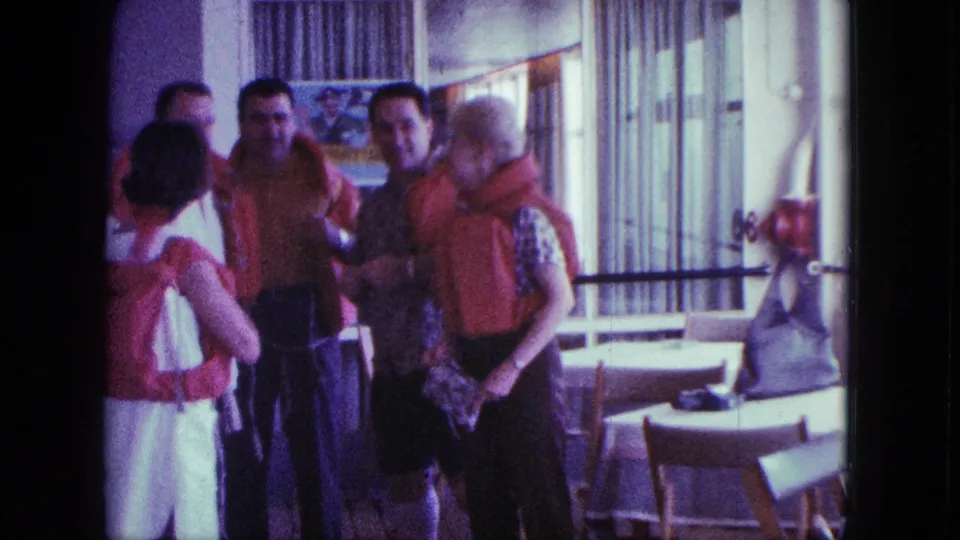 A small group in orange life jackets talks in a sunlit San Diego interior during a 1963 home movie.