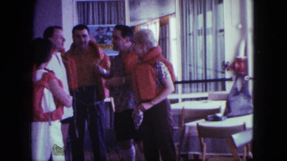 Adults in orange flotation vests converse and gesture in a 1963 San Diego boating-preparation scene.