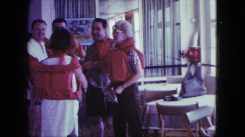 The group remains clustered in orange life jackets inside a bright room, consistent with 1963 San Diego boating footage.