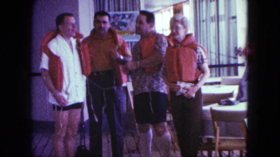 Four adults in a 1963 cruise-ship interior stand near windows and dining furniture while wearing or adjusting life preservers.