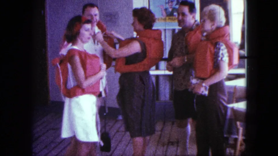 The group remains on the boat deck as a woman tightens or checks a life jacket in this 1963 San Diego home-movie frame.