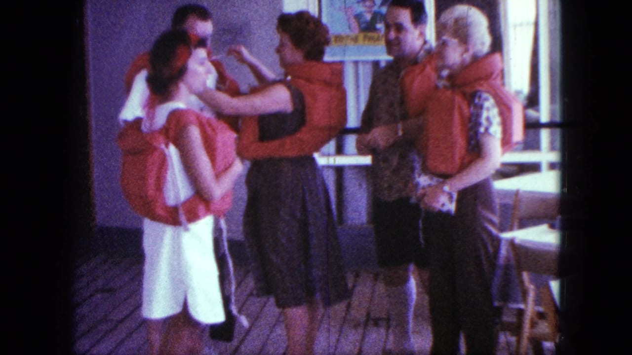 Adults on a wooden deck wearing red life jackets while a woman adjusts another person's jacket.