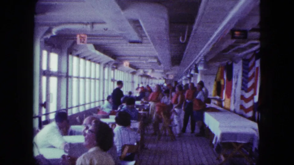 People in red life jackets move through the boat interior while other passengers sit near tables and windows.
