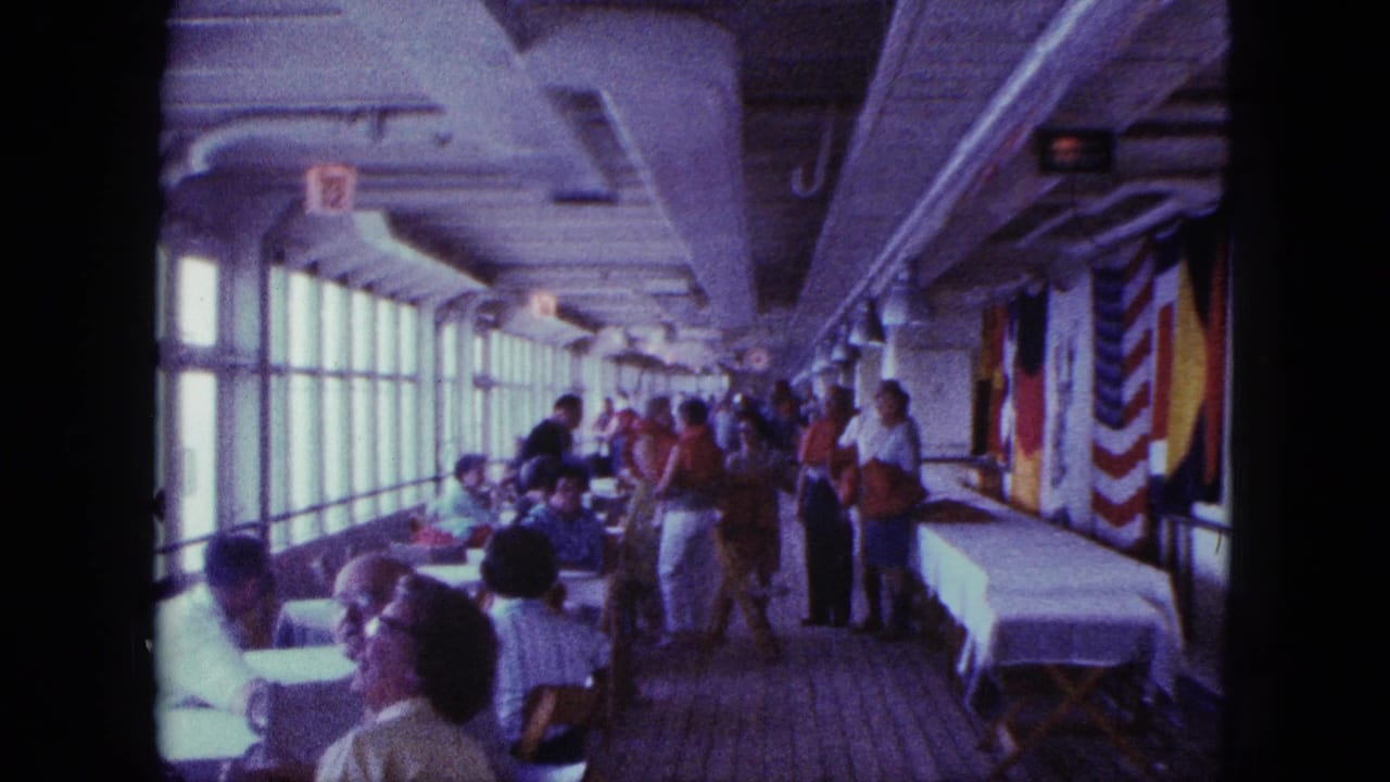 Adults sit and stand on an enclosed deck beside windows and a white-covered table.