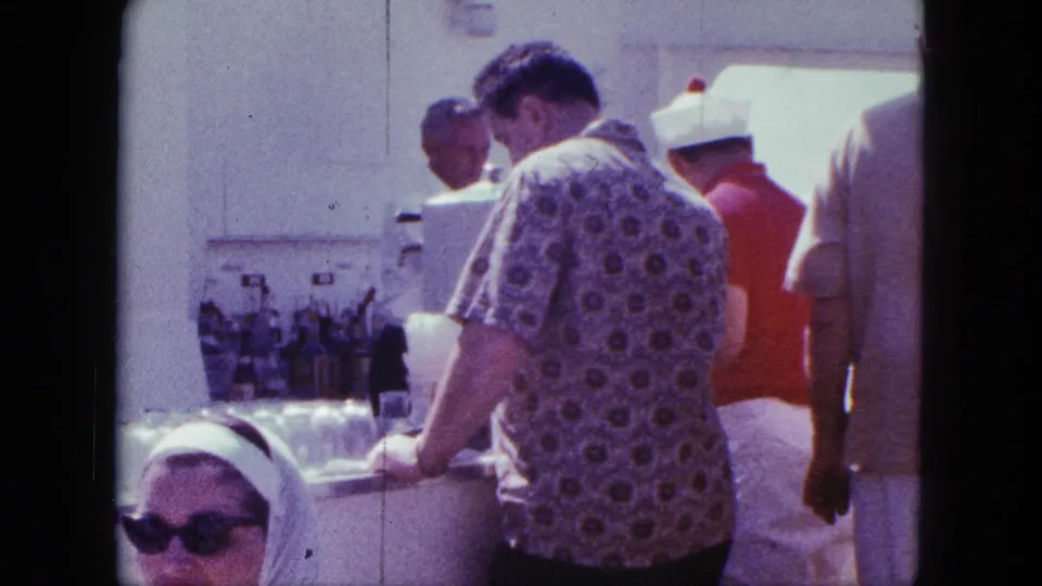 Shipboard buffet scene with adult passengers serving themselves, including a man in a patterned shirt and a woman in sunglasses and a headscarf.