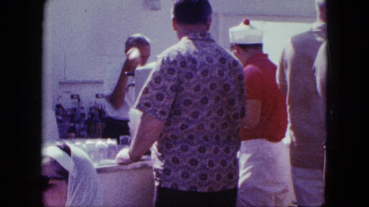 1963 San Diego home-movie frame showing men at a crowded outdoor counter with a vendor in a white cap and red shirt.