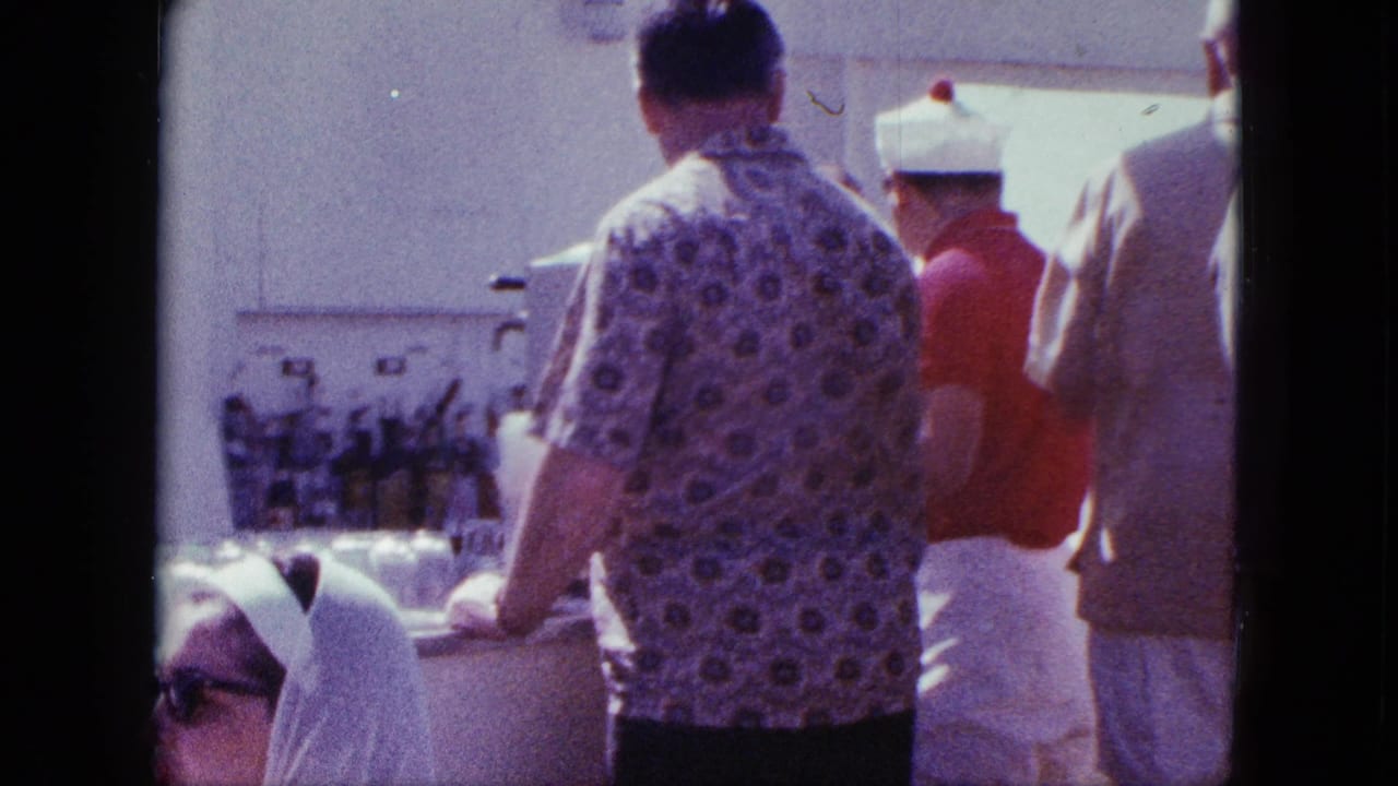A man in a patterned shirt stands at the counter near a vendor in a white cap.