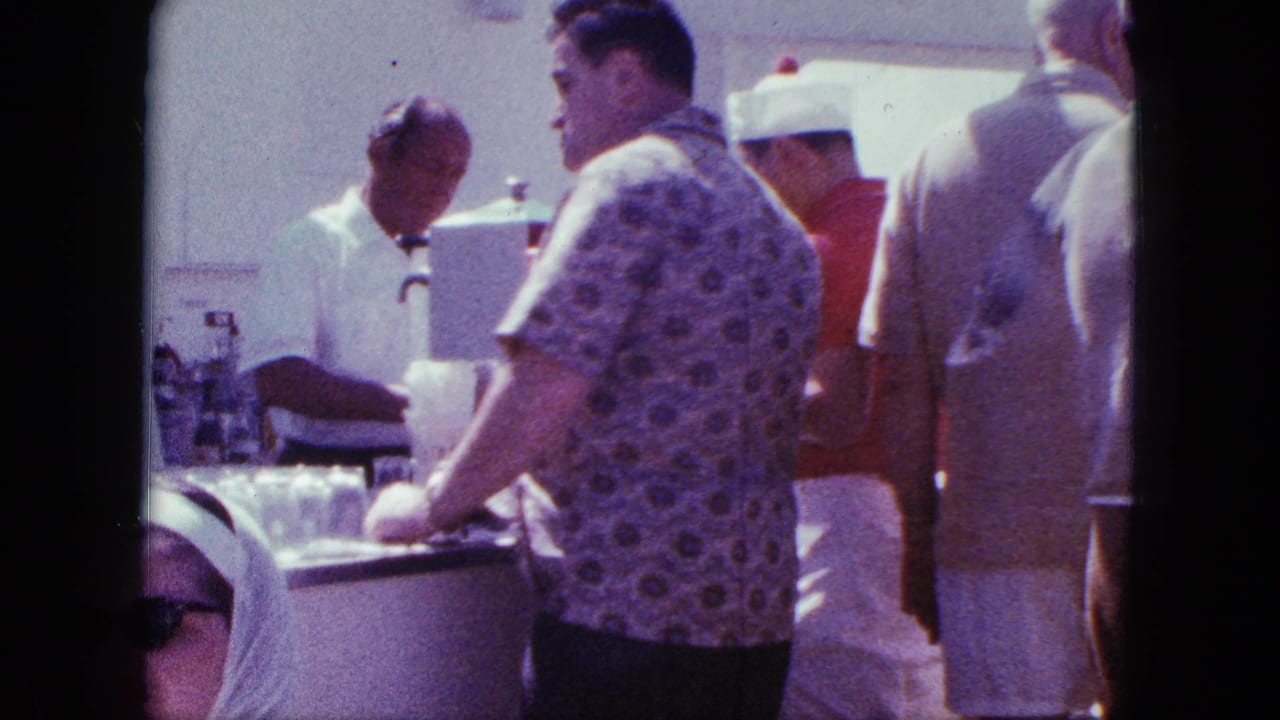Man in a patterned shirt stands at the counter as the bartender serves nearby.