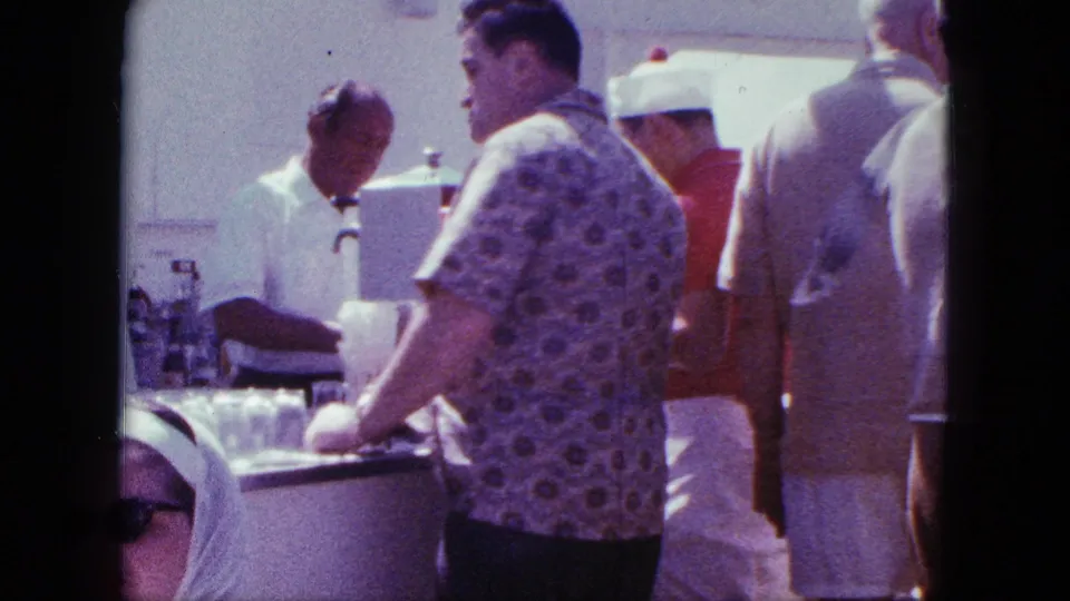 A man in a patterned short-sleeve shirt waits at a San Diego bar or grill counter while the white-uniformed bartender serves customers.