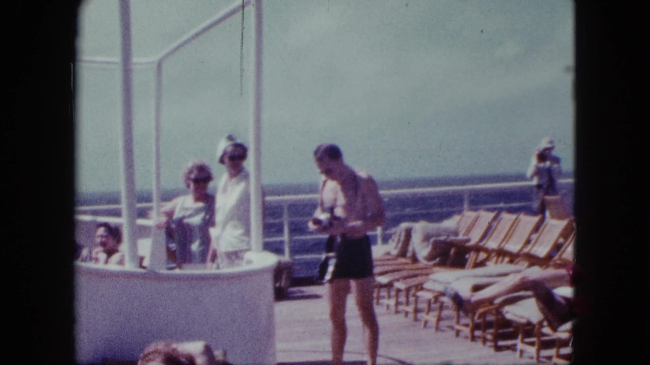 On the 1963 cruise deck, a shirtless passenger holds a camera while others stand or sit near lounge chairs and the ocean railing.