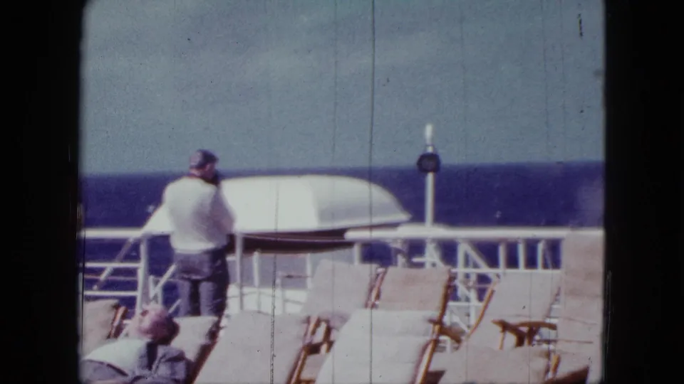 1963 cruise-liner deck footage showing a standing man near the rail, empty and occupied chairs, and the ocean beyond.