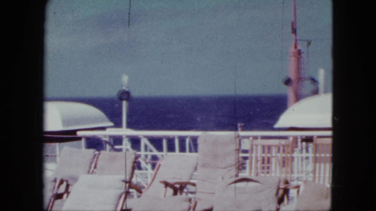 Ship deck with lounge chairs, white railing, ocean horizon, and a partial canopy.