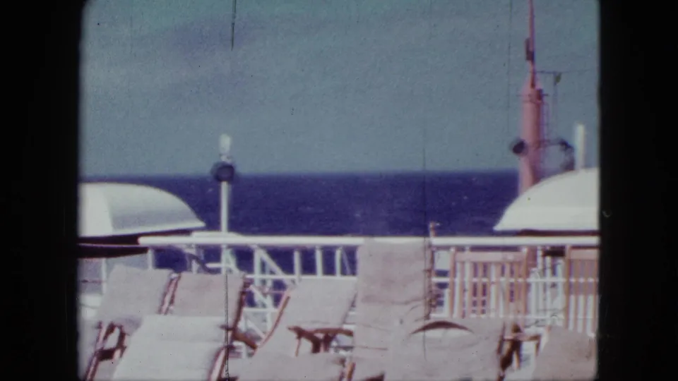 Cruise ship deck view with empty lounge chairs, white railings, ocean horizon, and ship fixtures in a 1963 home-movie frame.