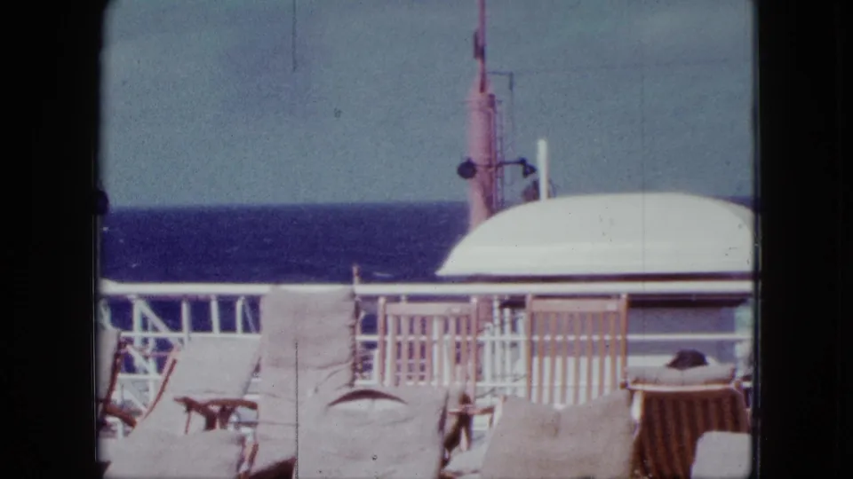 1963 cruise deck frame showing lounge chairs, white railings, curved canopy, ship fixture, and the ocean horizon beyond.