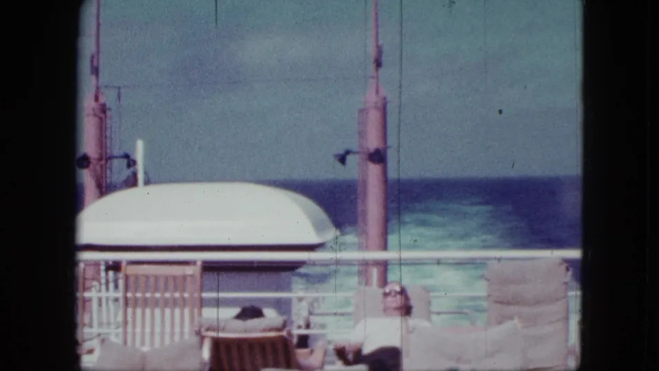 1963 San Diego boat-deck scene with a seated passenger in sunglasses, lifeboat housing, railings, and blue ocean in the background.