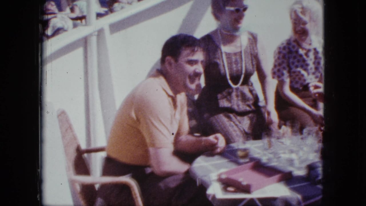 Adults seated around a table with drinks on a sunny deck.