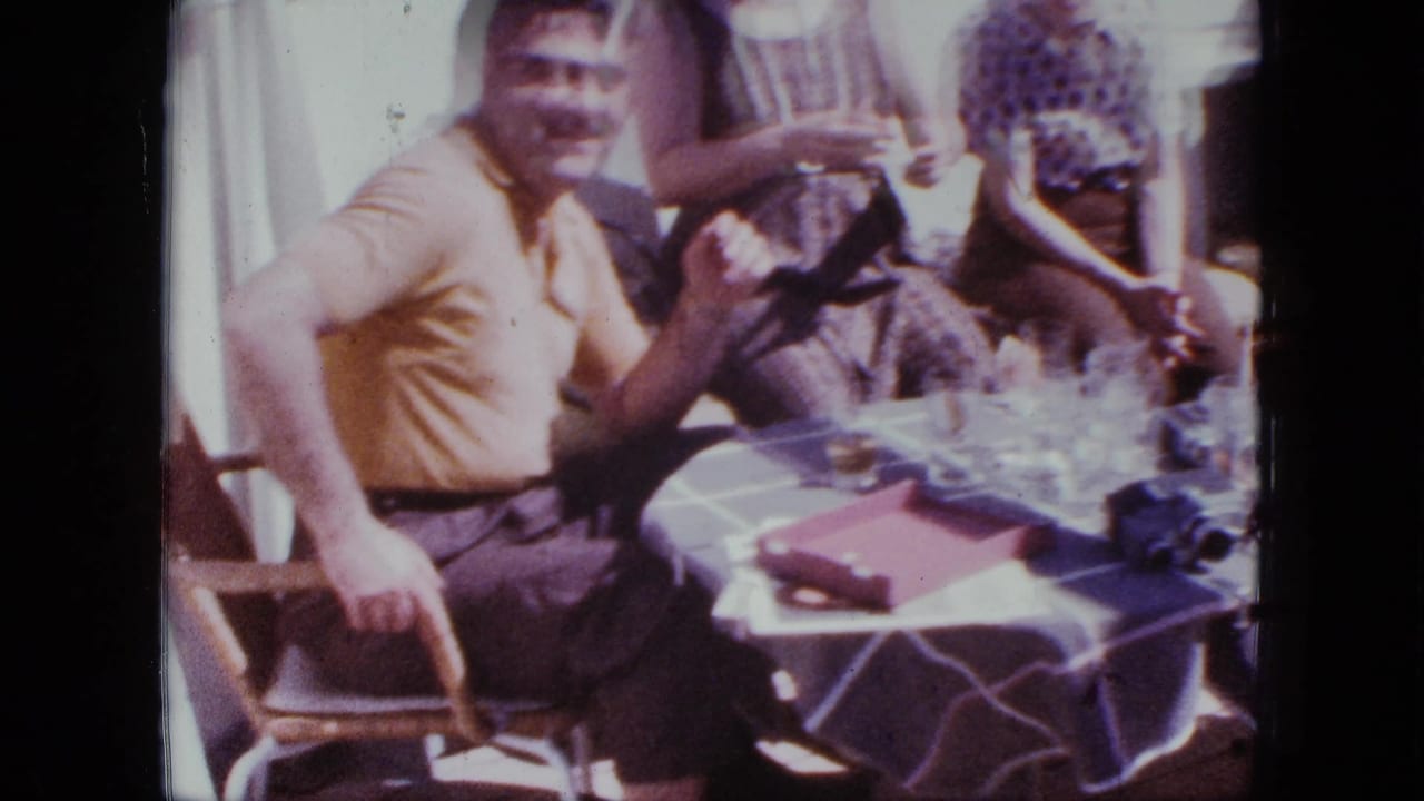 Adults sit around a checkered table on a boat while a man in a yellow polo smiles toward the camera.