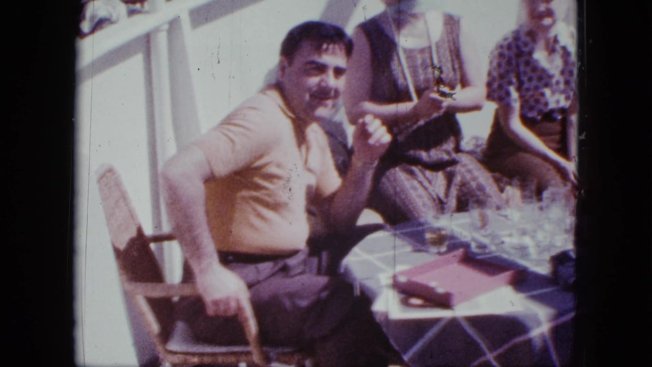 1963 San Diego boat scene with a seated man gesturing near glasses and a folded red item on a checkered table.
