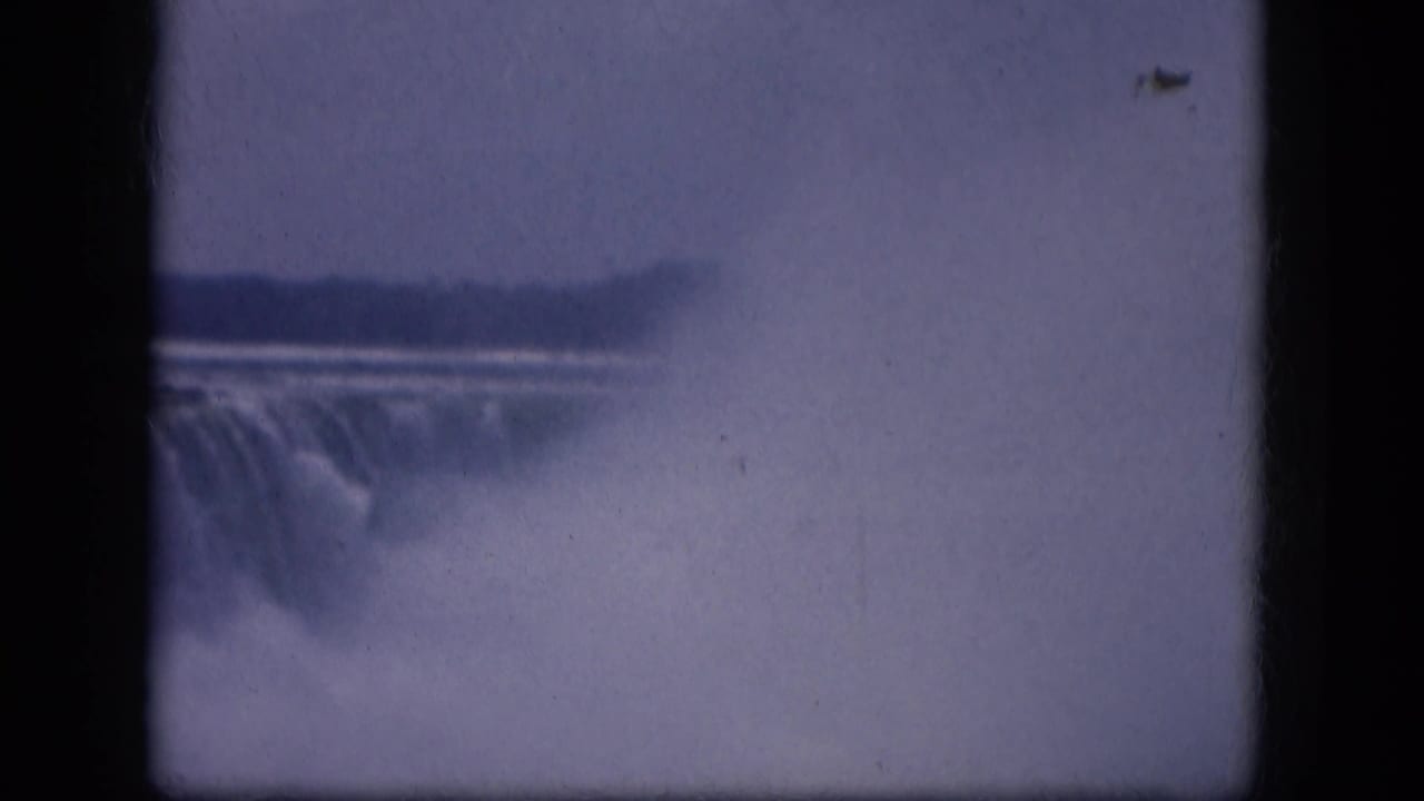 1964 8mm view of a misty waterfall in New York State, framed by dark gate edges and soft blue-purple film color.