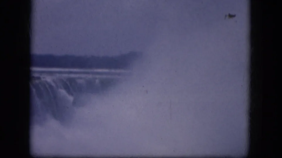 1964 8mm view of a misty waterfall in New York State, framed by dark gate edges and soft blue-purple film color.