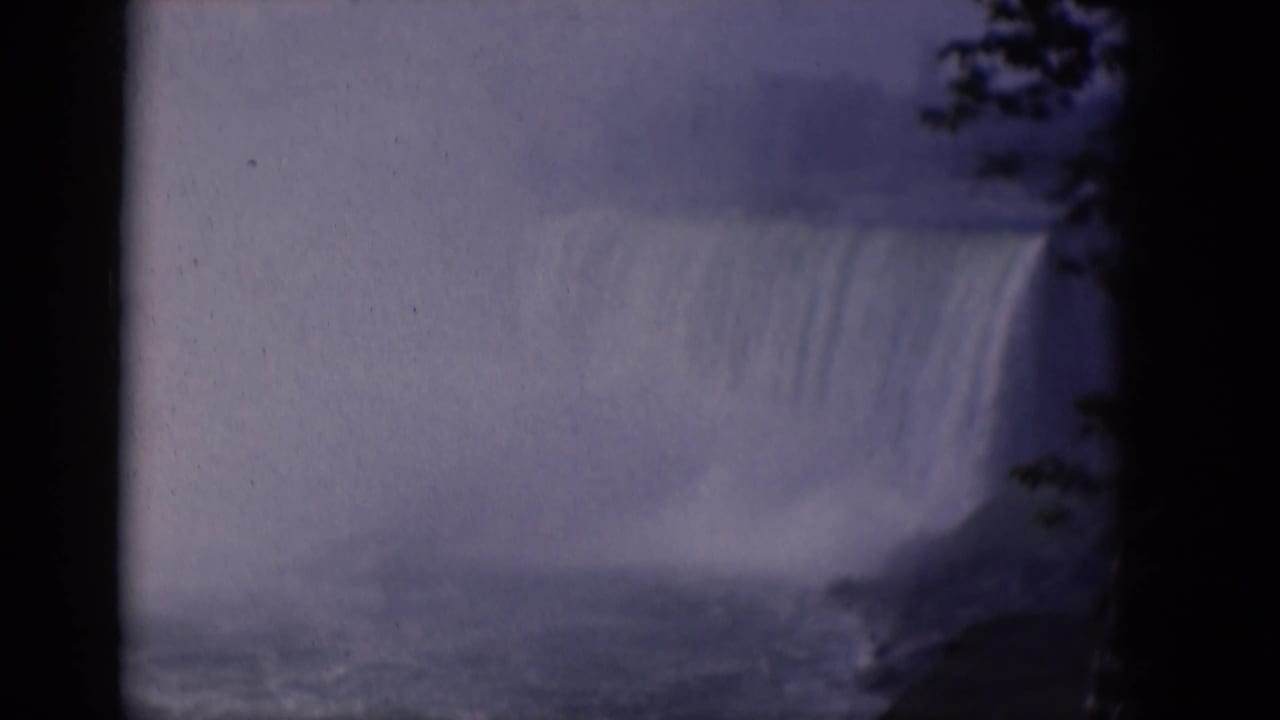 Misty waterfall with turbulent water below and dark foliage at the edge.