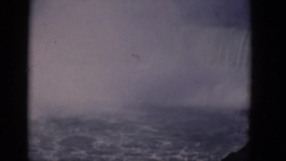 Soft 1964 8mm home-movie view of a large waterfall fading into mist, with rippled water below and dark edges from the film frame.