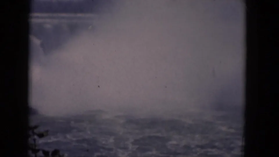 A distant 1964 home-movie view of Horseshoe Falls, with heavy mist, river texture, and a dark vertical frame division.