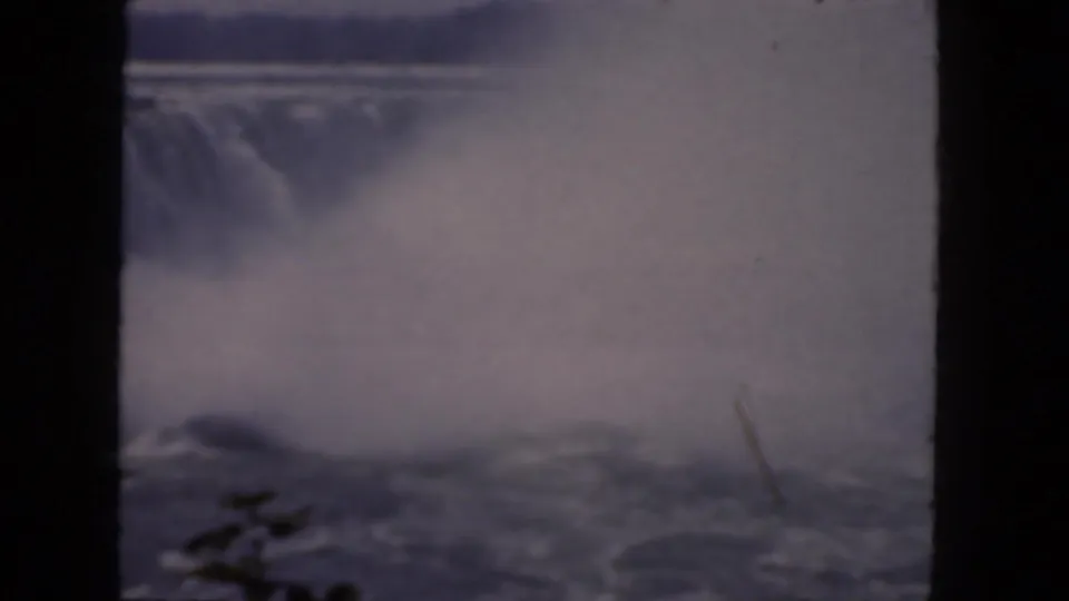 1964 8mm frame showing the Horseshoe Falls crest and dense spray, tinted blue-purple by aged home-movie film.