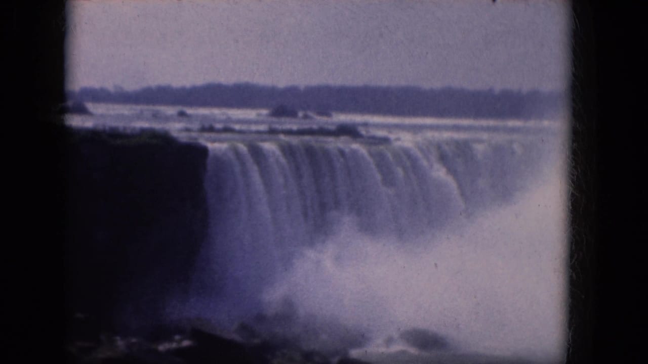Water pours over Niagara Falls with a large mist cloud rising below the cliff edge.