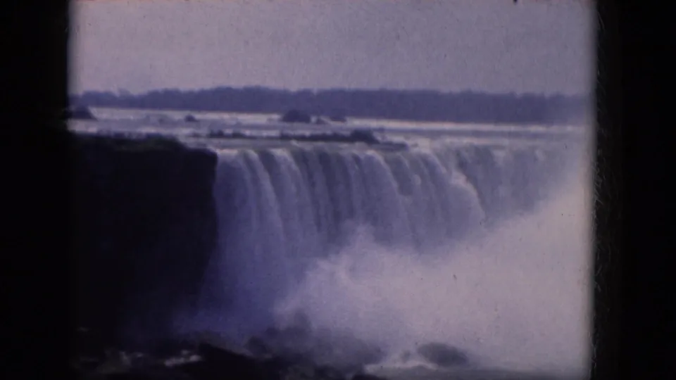 1964 8mm home-movie view of Niagara Falls, with water dropping over a dark cliff and mist rising under an overcast sky.