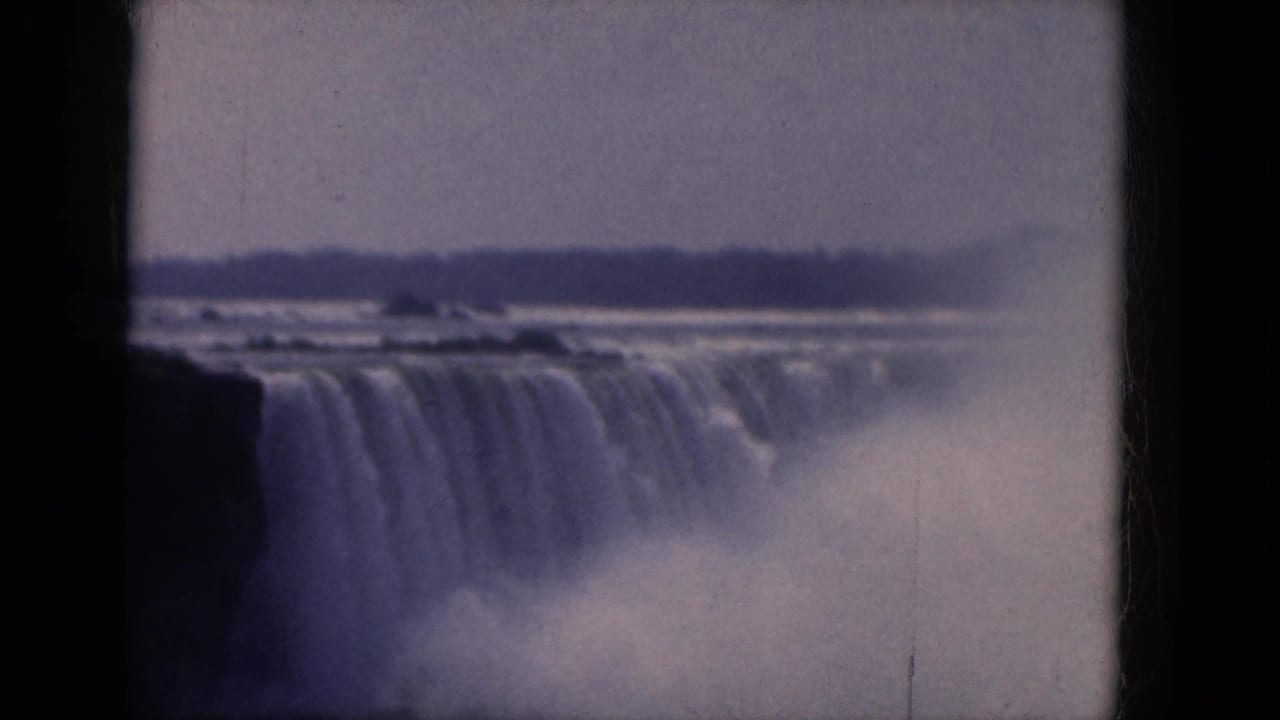 Canadian-side Niagara Falls view on 8mm film, showing a broad cascade, river mist, and a low distant shore.