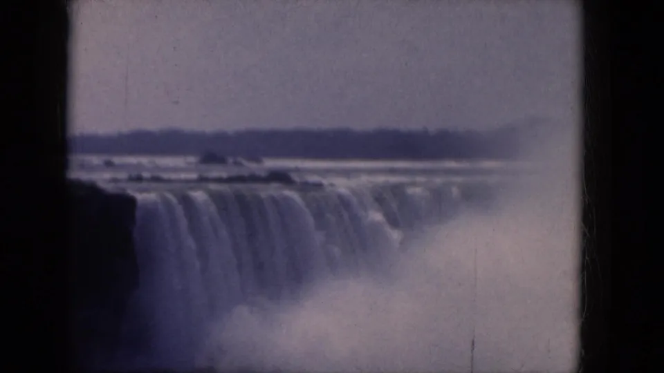 Canadian-side Niagara Falls view on 8mm film, showing a broad cascade, river mist, and a low distant shore.