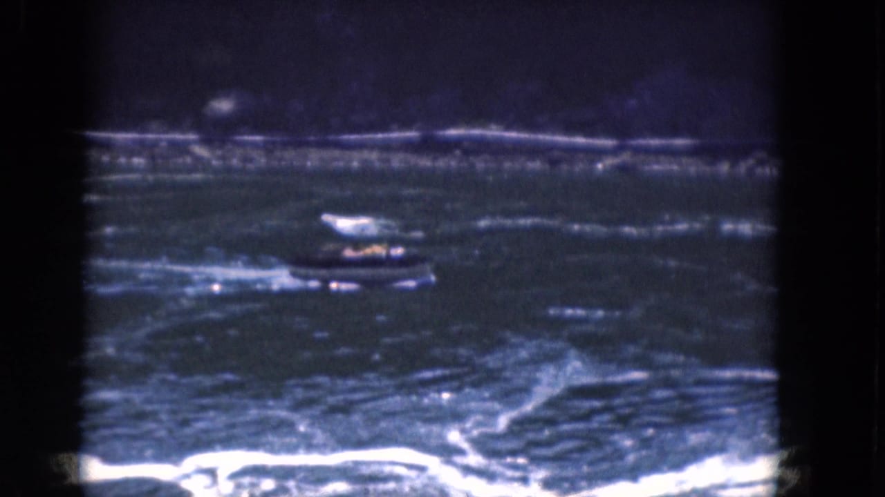1964 Albany-area home-movie frame of a small boat on rough water, seen through soft blue 8mm film texture.
