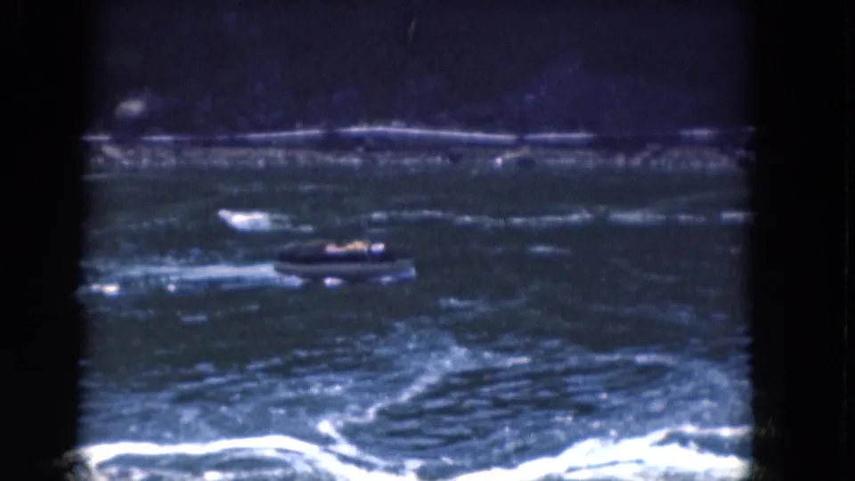 1964 Albany-area home-movie frame showing a small motorboat above bright wake lines on choppy water.