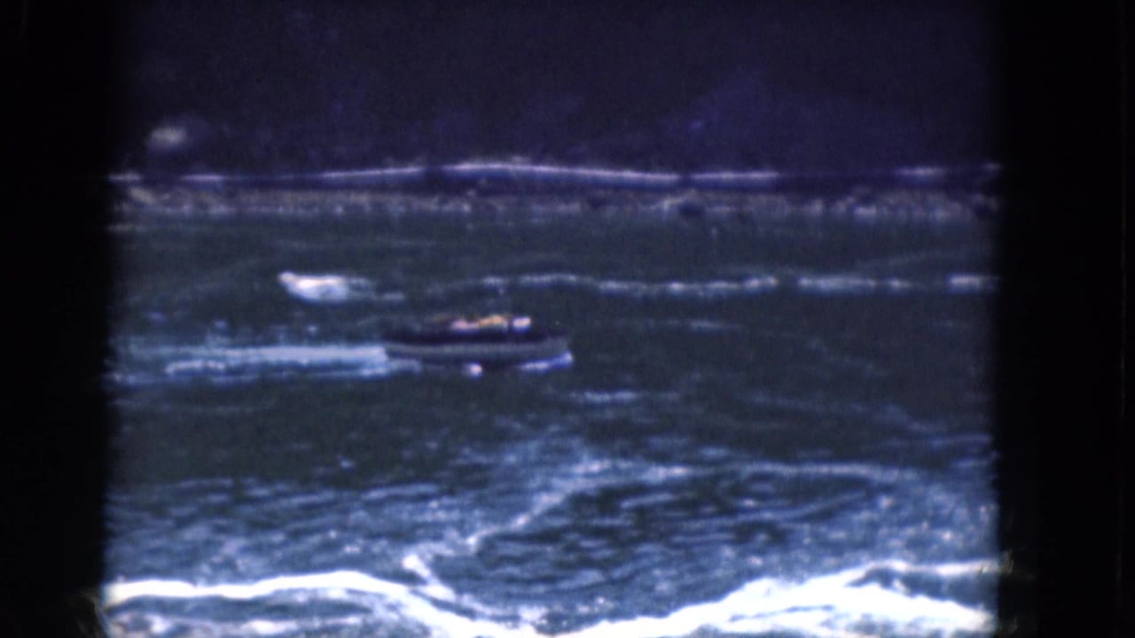 Small motorboat crossing choppy blue water with whitecaps and a dark shoreline behind it.