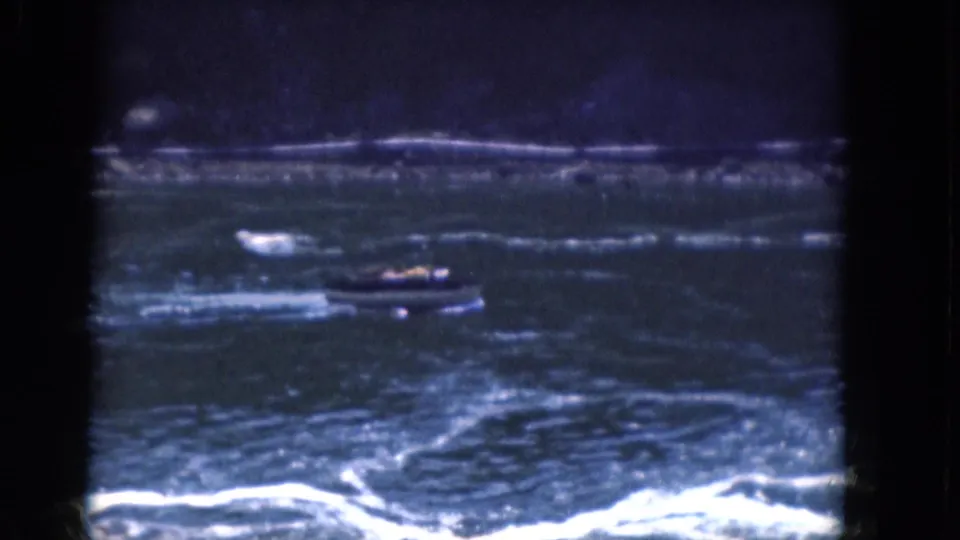 1964 8mm frame from Albany, New York metadata showing a small motorboat on rough blue water with white foam and a distant dark shore.