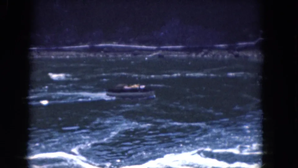 1964 8mm home-movie frame showing a small motorboat on choppy water near Albany, with white foreground foam and a distant shore.
