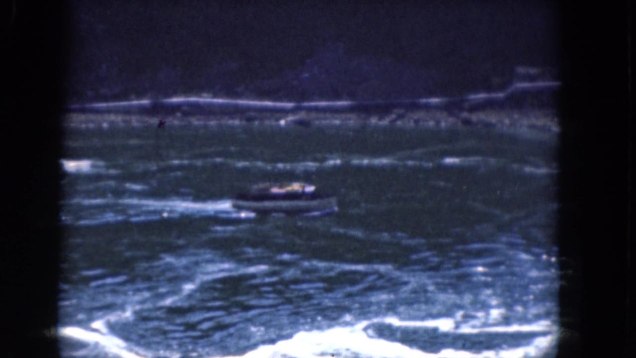 Small motorboat crossing choppy river water with a dark shoreline in the distance.
