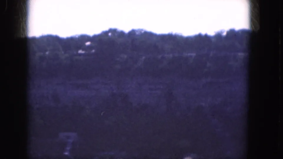 1964 Albany-area landscape frame with a dark film edge, pale sky, wooded ridge, and faint distant buildings or rooflines.