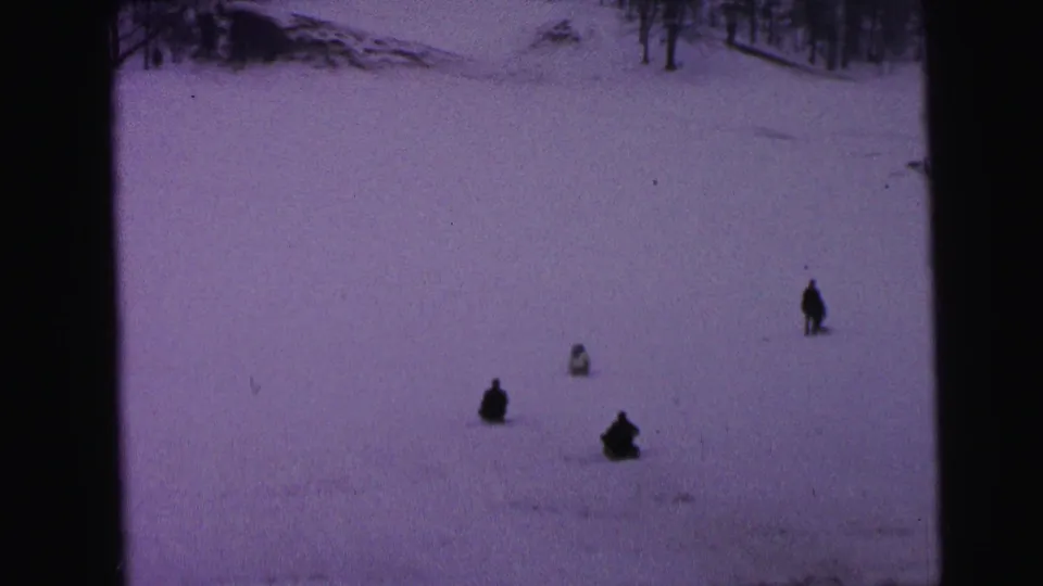 1964 Camden 8mm frame showing distant people sledding across a wide, purple-tinted snowy hill.