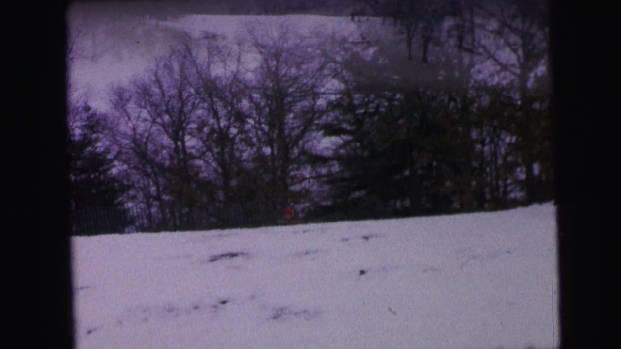 Snowy slope with bare trees and a small red figure near the treeline.