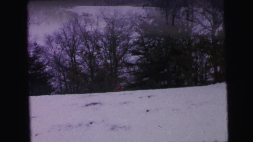 1964 Camden winter frame showing a snowy slope, bare woods, and a small red-clad sledder or figure near the trees.