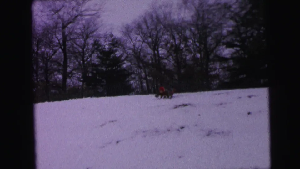 1964 Camden winter recreation frame showing a red-clad person on or near a sled descending a snowy hill with bare trees behind.