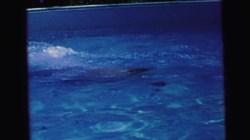 A swimmer is partly visible beneath reflective blue pool water in 1964 Camden, New Jersey home-movie footage.