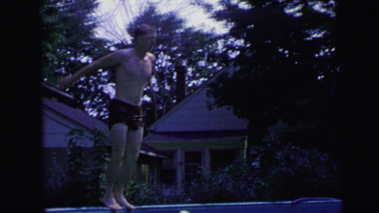 Young man in dark swim trunks standing at the edge of a backyard pool.