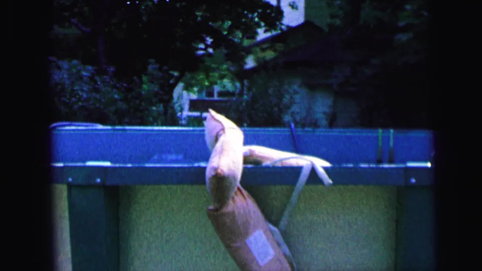 1964 Camden home-movie frame showing a pale life jacket or vest draped over the rim of an above-ground pool.
